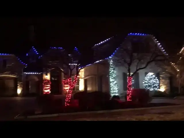 Home with blue and white roofline lights and a red lit tree at night