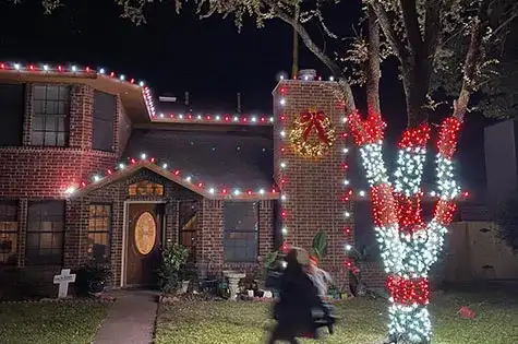 Brick home with roofline lights and red and white wrapped trees