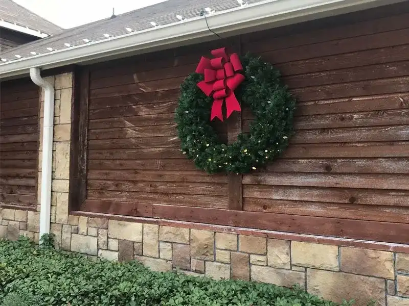 Large outdoor wreath with a red bow on a wood-sided home
