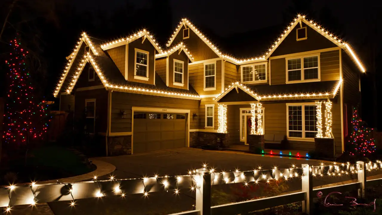 Craftsman home with warm white roofline lights and a lit white fence